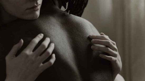 A woman embraces a topless man.