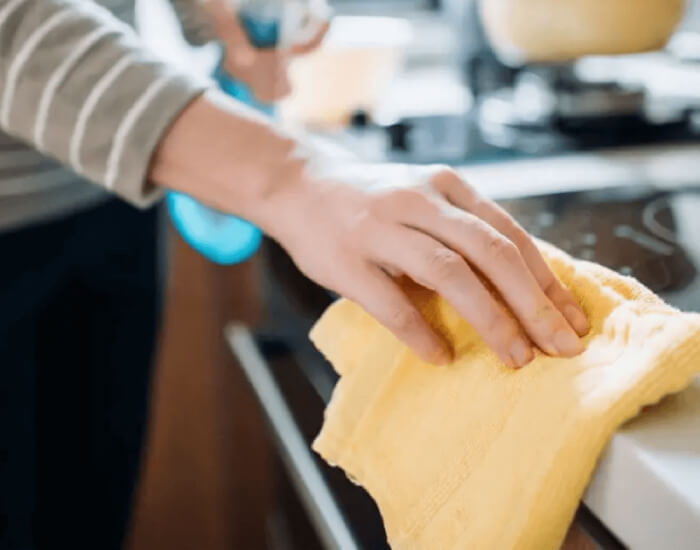 A person wipes a kitchen counter with a yellow cloth
