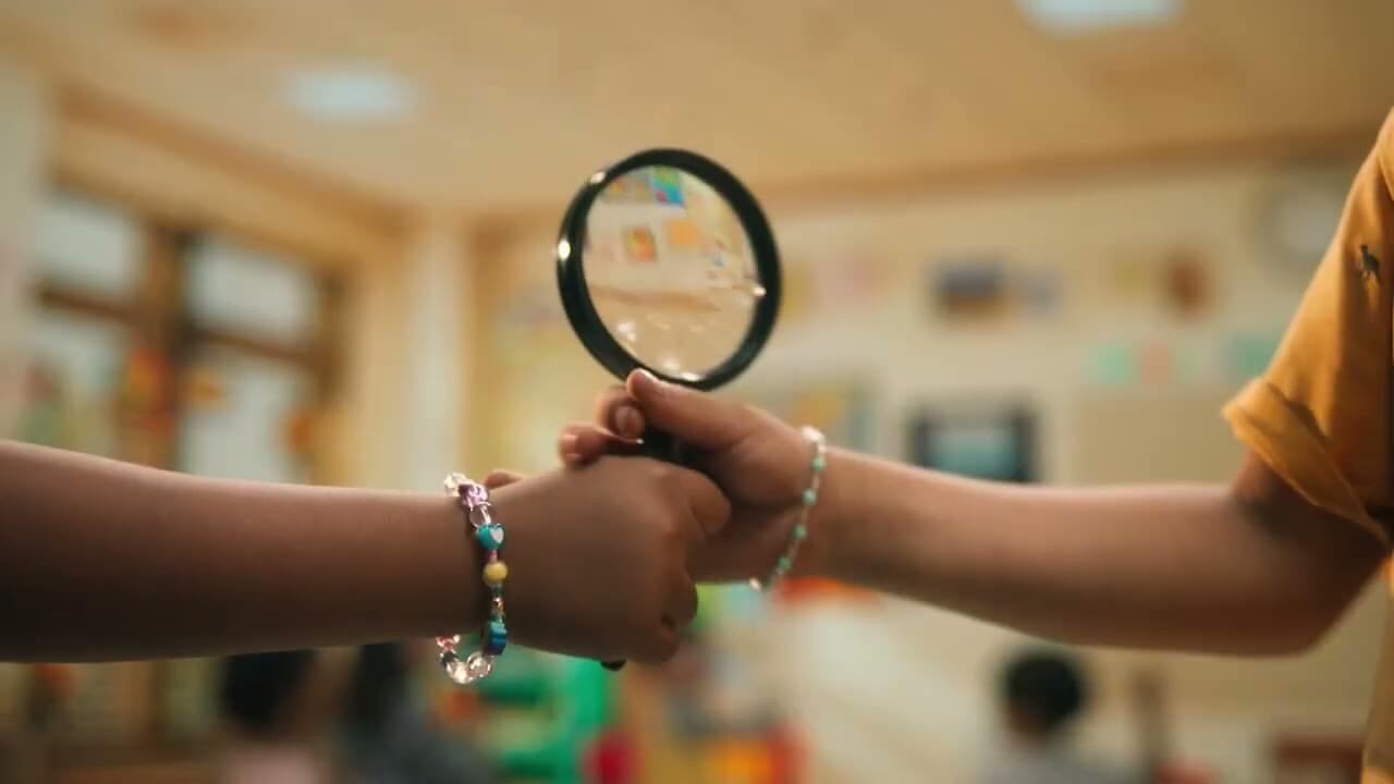 Two children holding a magnifying glass with beaded bracelets on their wrists.