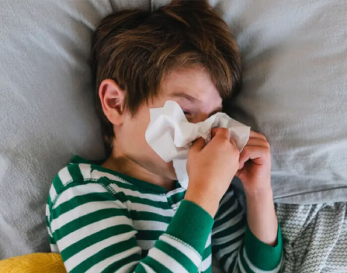 A child sick in bed holding a tissue to their nose