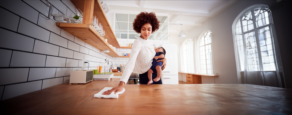 a woman cleaning a wooden kitchen counter while holding a baby