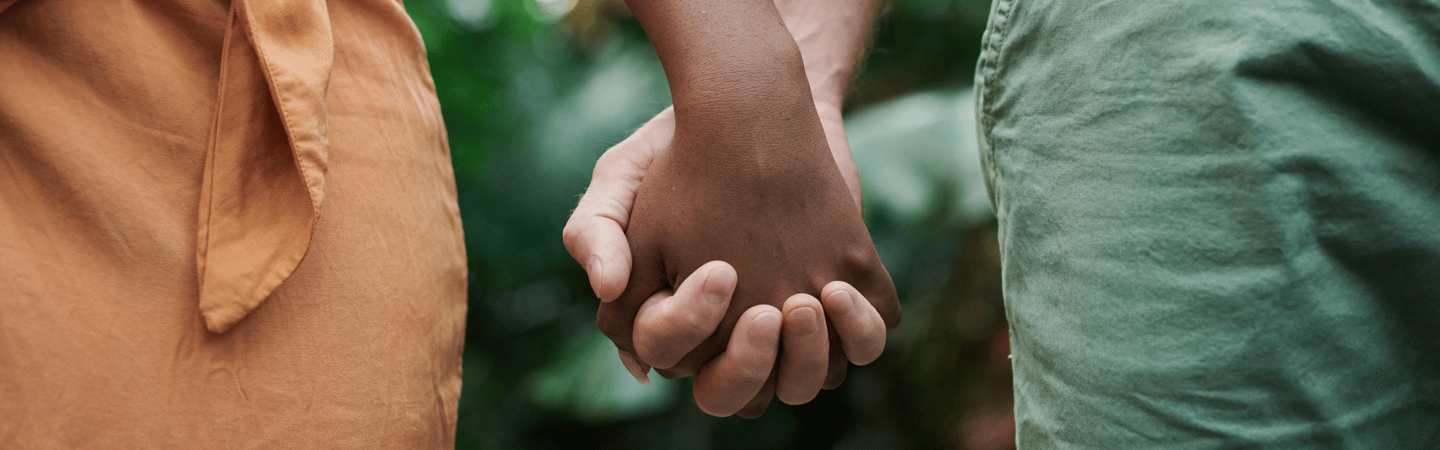 Close-up of two people holding hands, standing side by side outdoors with blurred greenery in the background, symbolizing connection and togetherness.