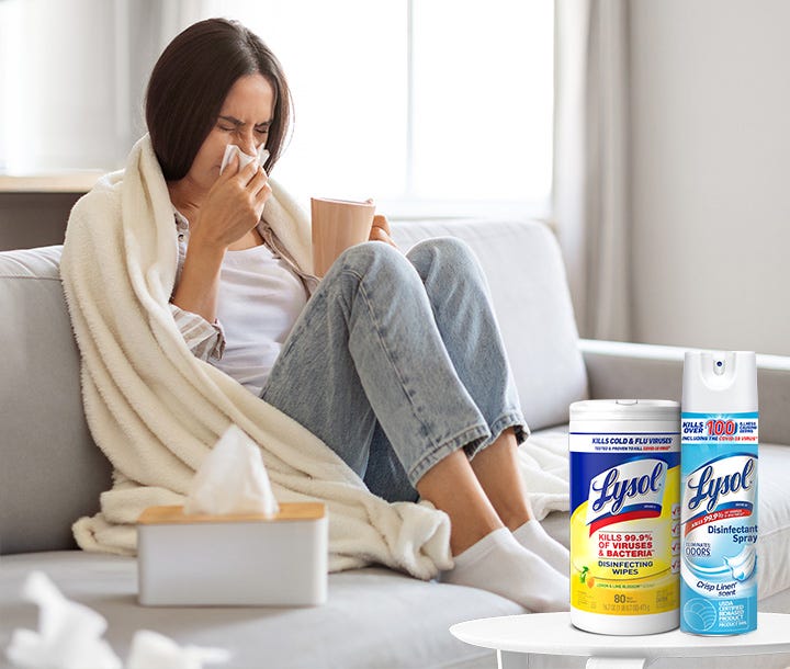 A person sitting on a sofa with tissues and Lysol products nearby.