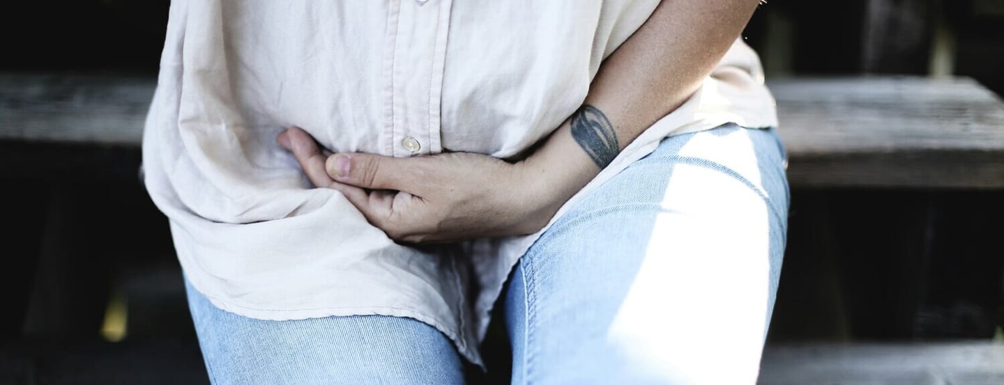 A woman grips her lower abdomen, suggesting physical discomfort or pain