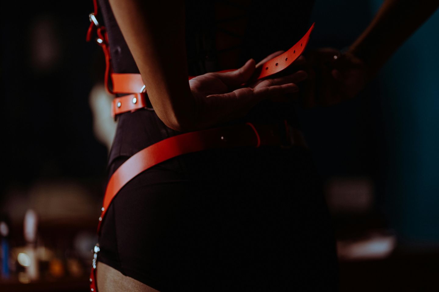 Pessoa vestindo acessórios de couro estilo bondage em ambiente com iluminação baixa.