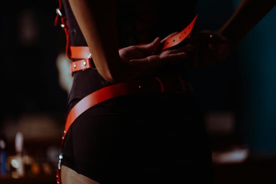 Pessoa vestindo acessórios de couro estilo bondage em ambiente com iluminação baixa.