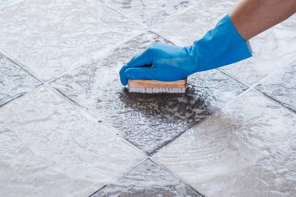 Hand of man wearing blue rubber gloves is used to convert scrub cleaning on the tile floor