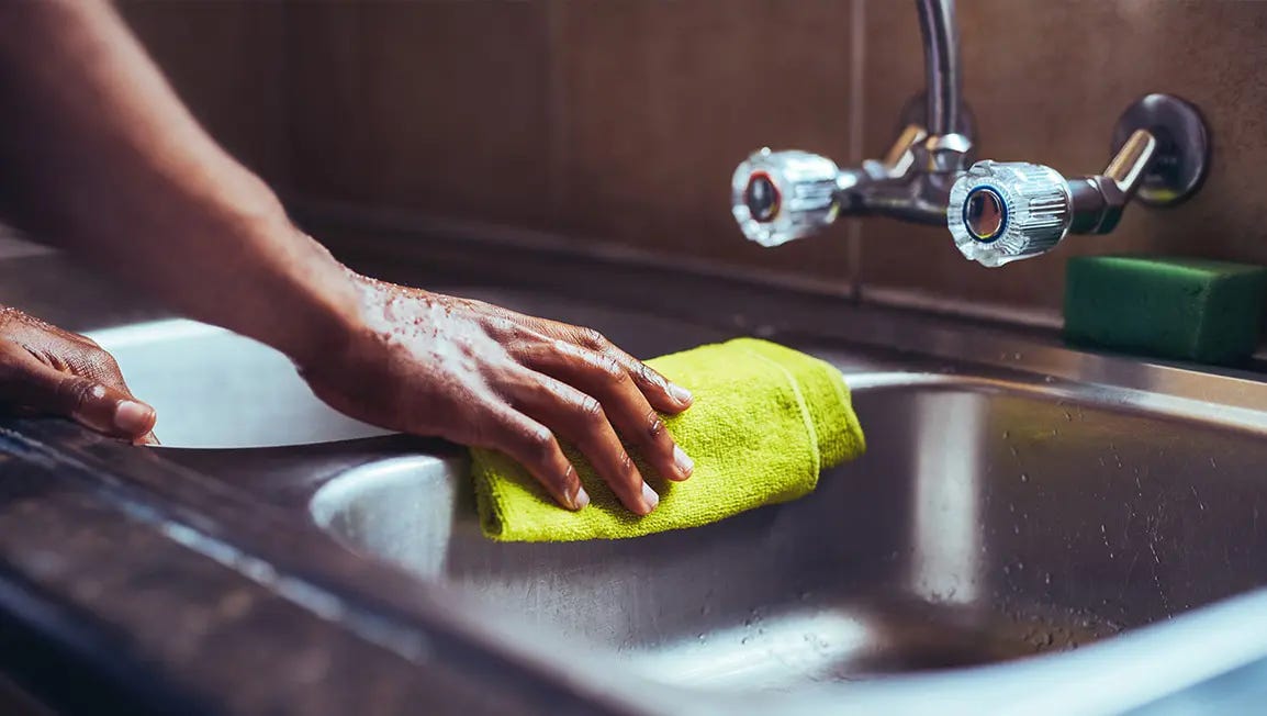 A hand cleaning a stainless steel sink with a yellow cloth.