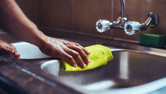 A hand cleaning a stainless steel sink with a yellow cloth.