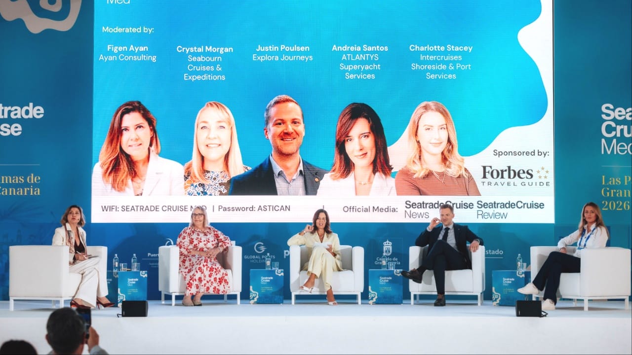 Four women and one man sat on white chairs on a stage
