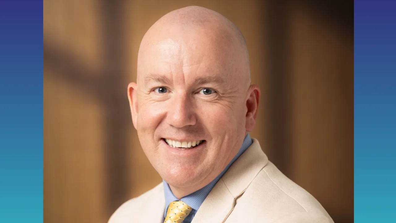 A smiling man wearing a yellow tie and cream blazer