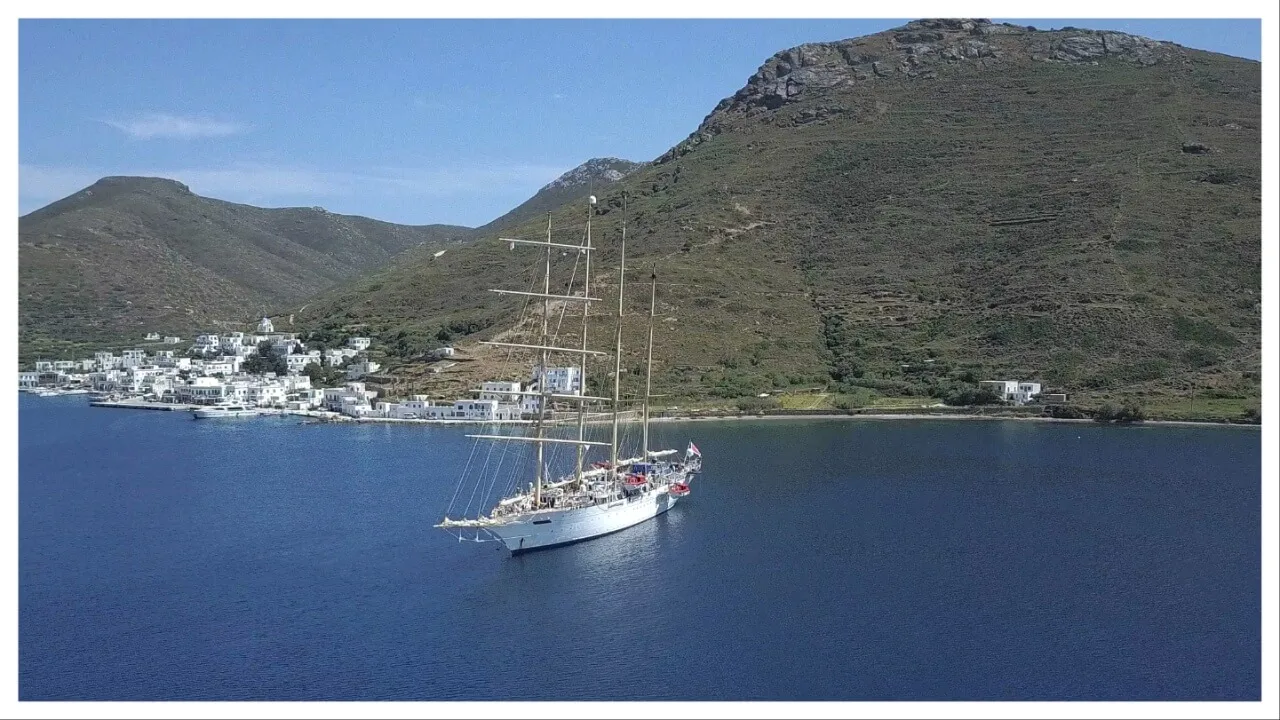 tall ship anchored off hilly coast and village of white buildings