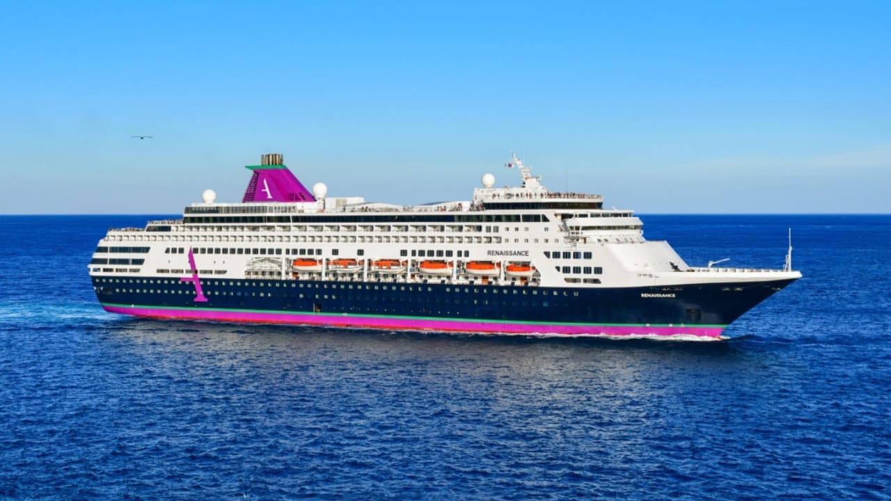 A white and blue cruise ship, with a purple funnel and keel, sailing on open ocean
