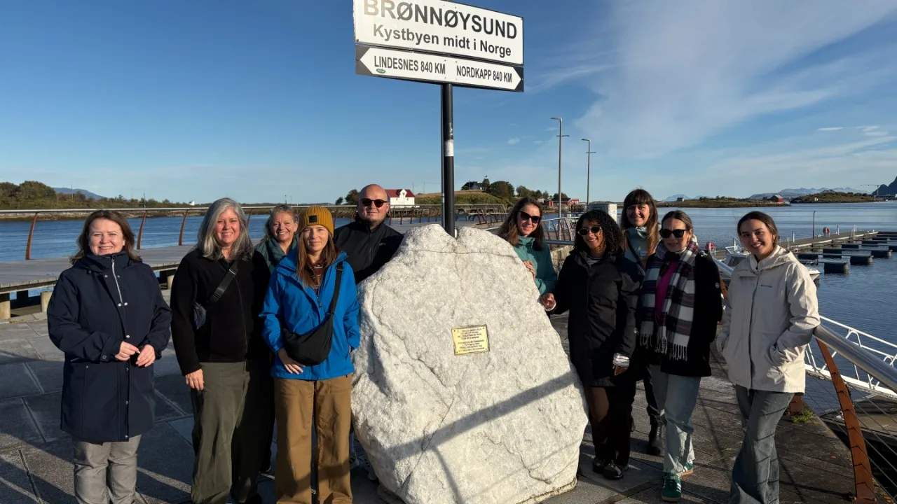 A group of smiling people in outdoor wear gathered around a large marble rock