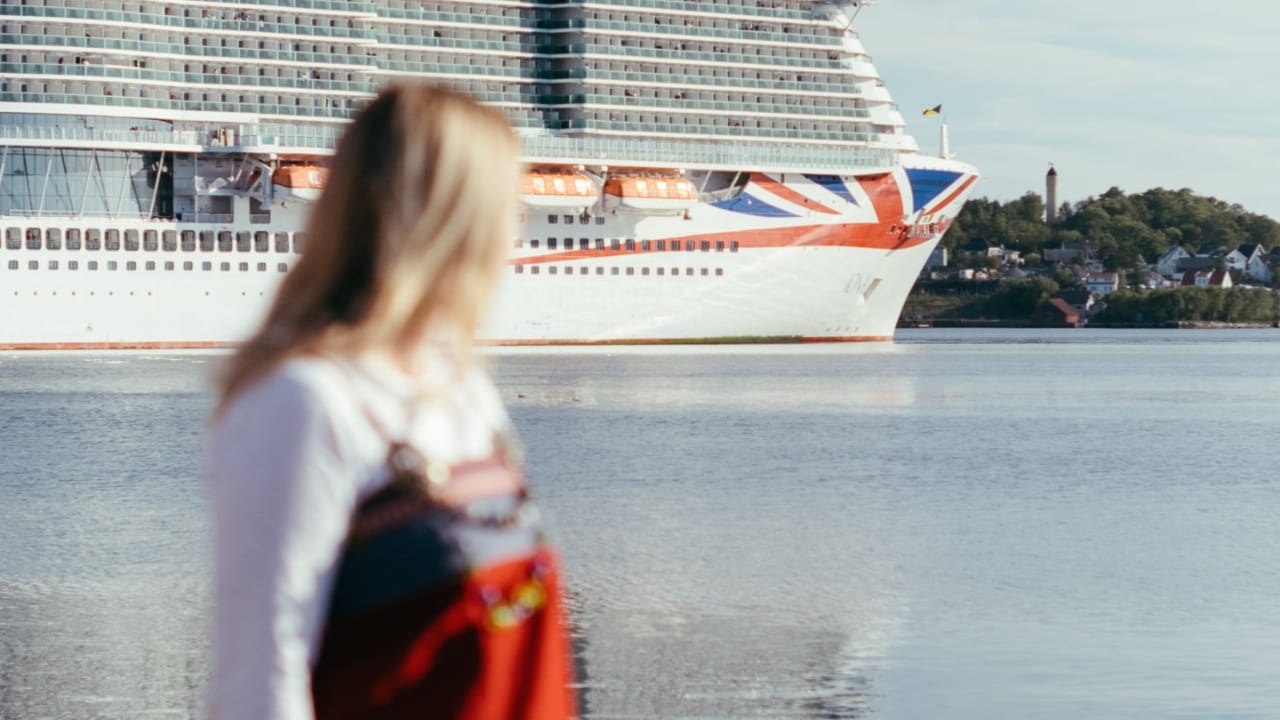 A woman with blonde hair wearing a red, white and black dress stood in front of a cruise ship on water