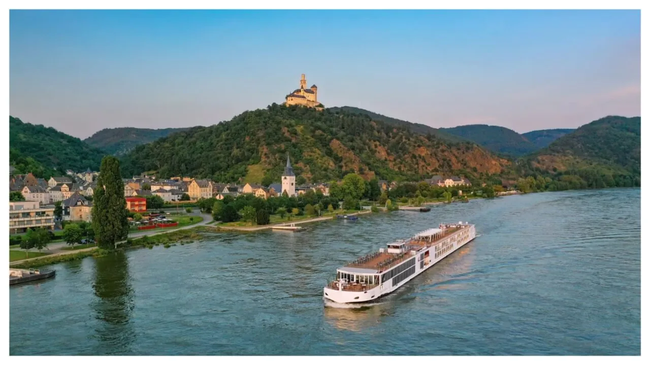 embarcação de cruzeiro fluvial navega por uma vila com campanário de igreja e castelo numa colina