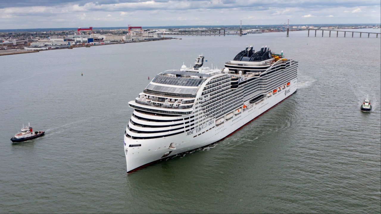 Un gran crucero blanco navega en mar abierto flanqueado por dos remolcadores