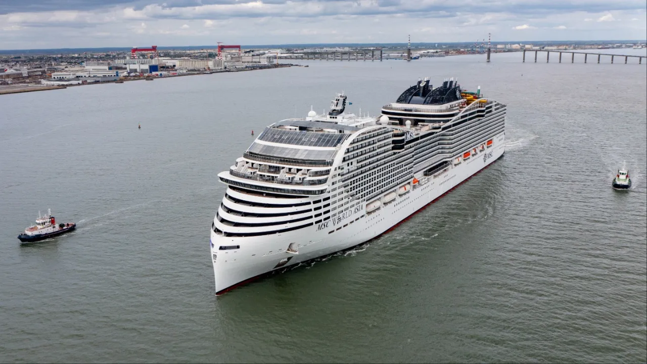 Un gran crucero blanco navega en mar abierto flanqueado por dos remolcadores