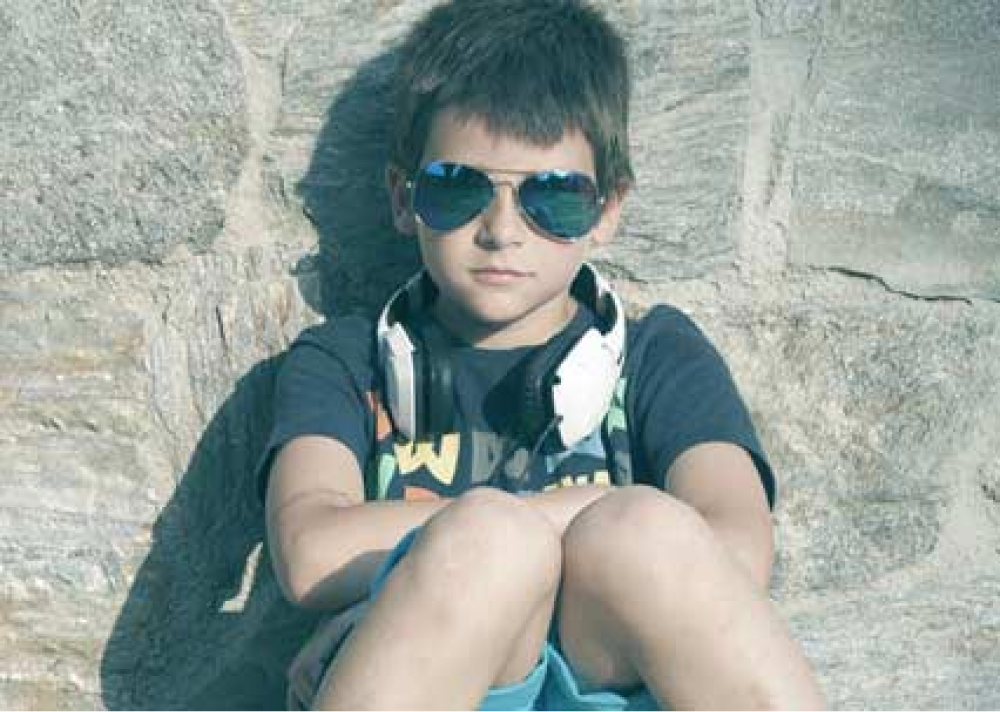 Pojke med solglasögon sittandes med hörlurar runt halsen