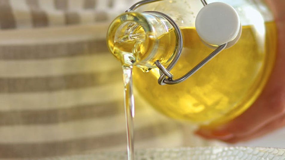 A person pouring cooking oil from a glass jar into a bowl