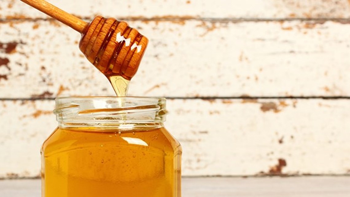 A jar of honey with a honey dipper dripping honey