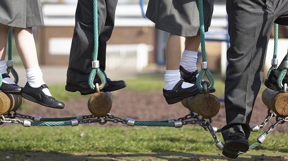Children in school uniforms balancing on logs connected by ropes