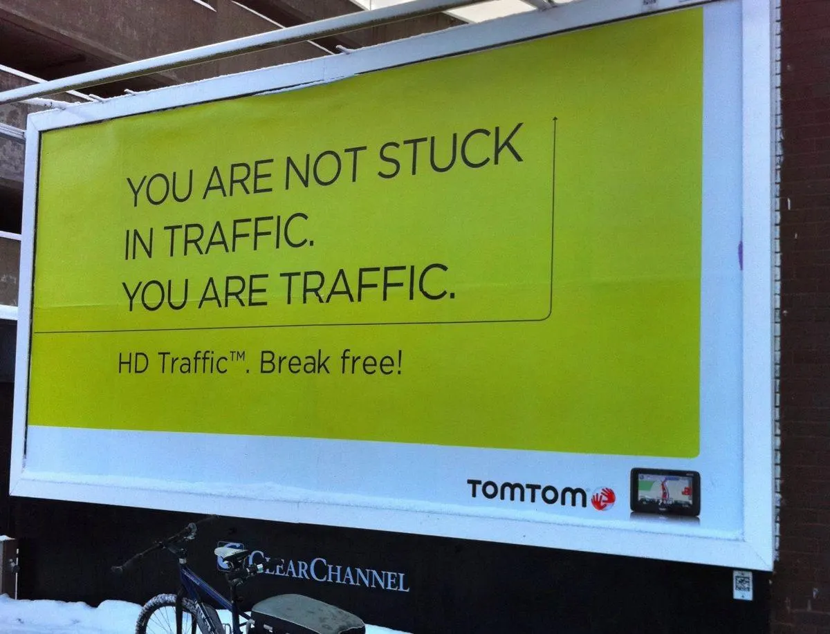 Billboard ad for TomTom GPS with a bold yellow background. The text reads: 
