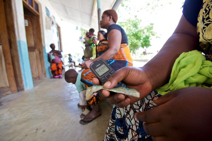Tanzanian women sat with mobile phones waiting to charge them at a solar-powered charging booth, Miono Region, Tanzania.