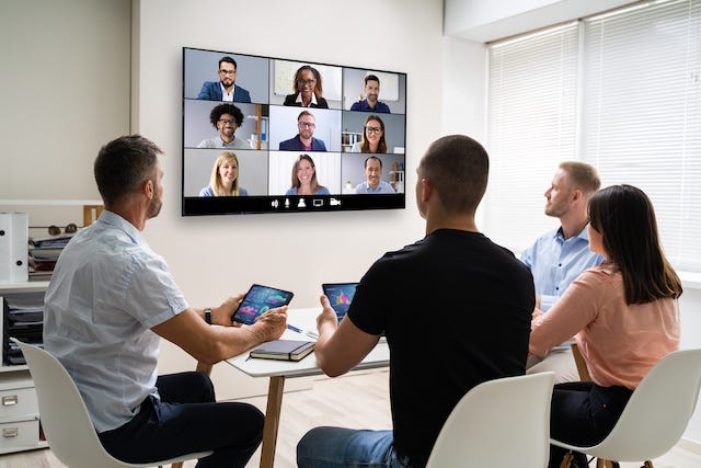 An online video meeting with people sitting around a conference room table.