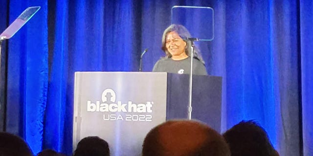 Supriya Mazumdar, with medium length black hair and a gray t-shirt, stands at a Black Hat USA 2022 podium