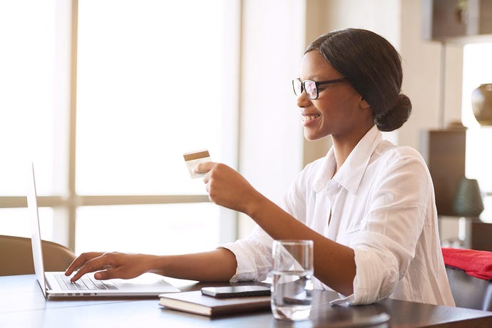 Photo of a young Black woman smiling as she types her credit card information into her laptop computer
