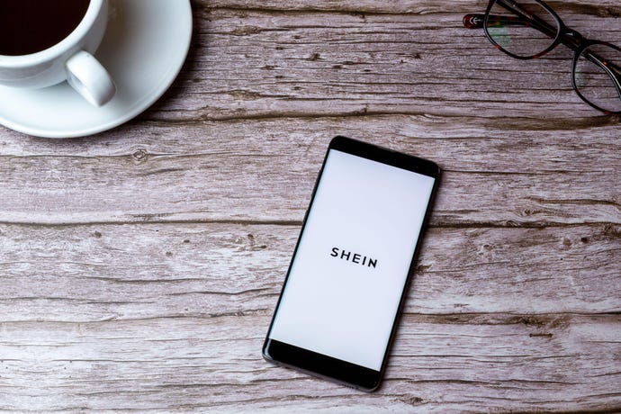Shein app on the screen of a cellular device laying on a wooden table.