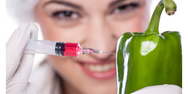 Photo of a woman smiling as she injects red fluid into a green pepper
