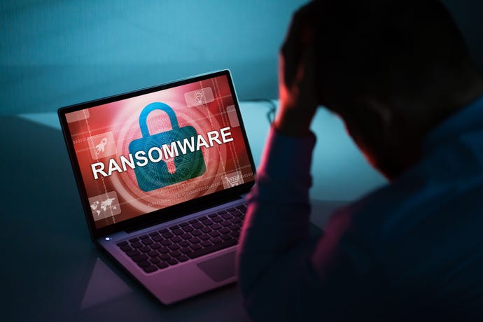Image shows a computer screen showing the word "Ransomware" and a man at it in a shadow with his hand on his head