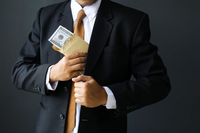 Concept for corruption, hacking for hire; a man tucks an envelope of hundred-dollar bills into his suit pocket
