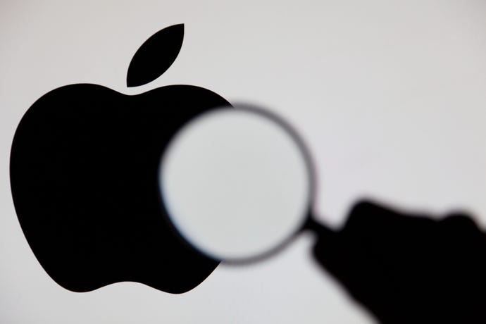Silhouette of a hand holding a magnifying glass in front of the Apple logo