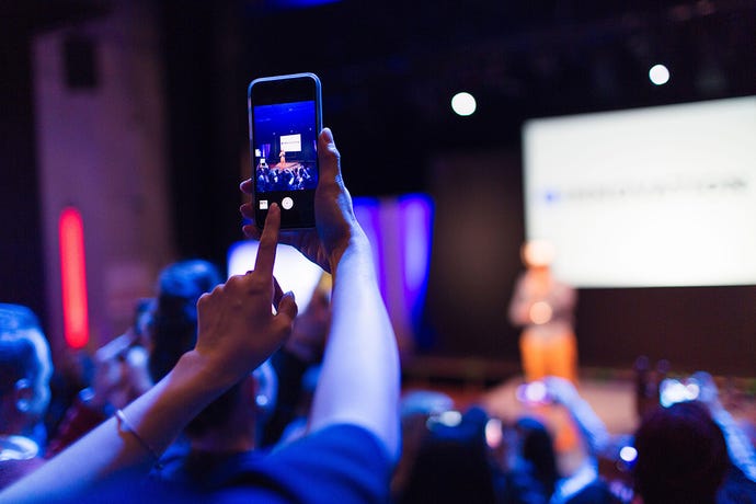 Photo of an audience member taking a photo of a conference presentation with their cell phone