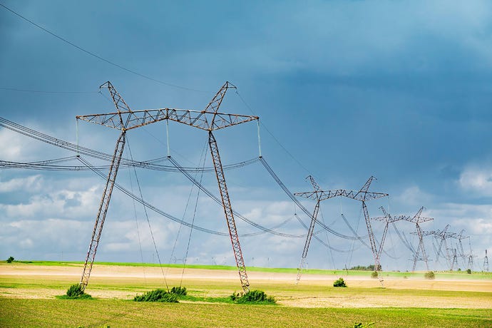 Row of power line support pylons in the yellow fields of Ukraine, against a blue sky