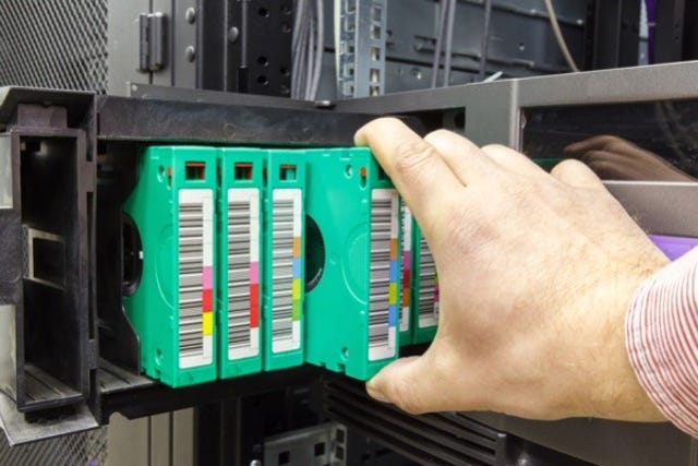 A white man's hand removes a tape backup from a rack of backups