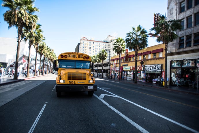 School bus driving down LA street lined with palm trees