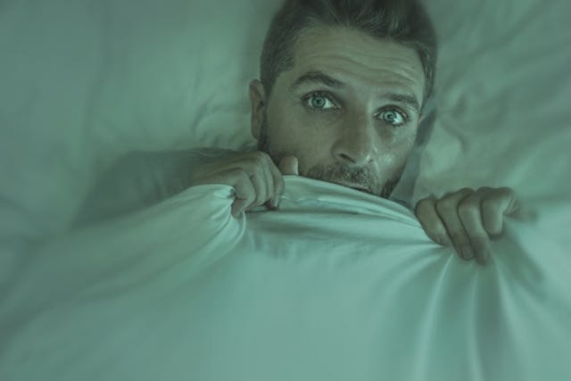 Man hiding under the covers, looking scared as if he had a nightmare.