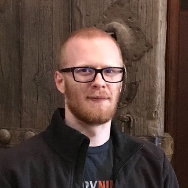 Brandon Falk, a man with a short red beard, dark-framed glasses, and dark shirt