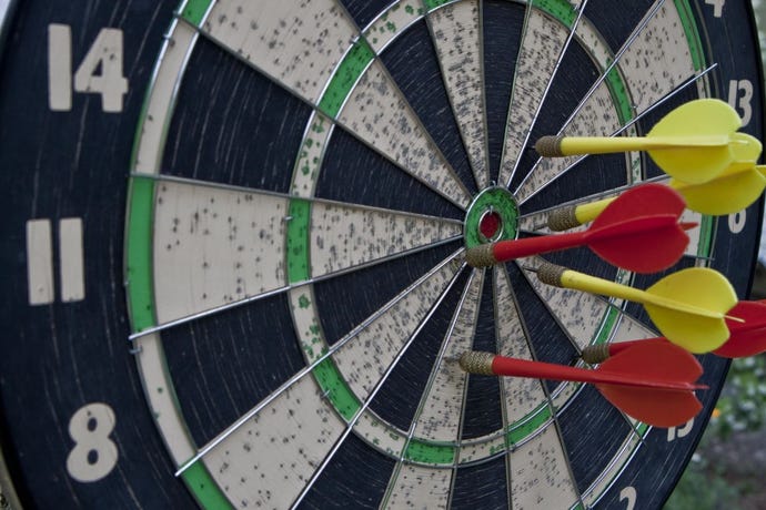 Image of darts target with six arrows hanging on red wooden wall.