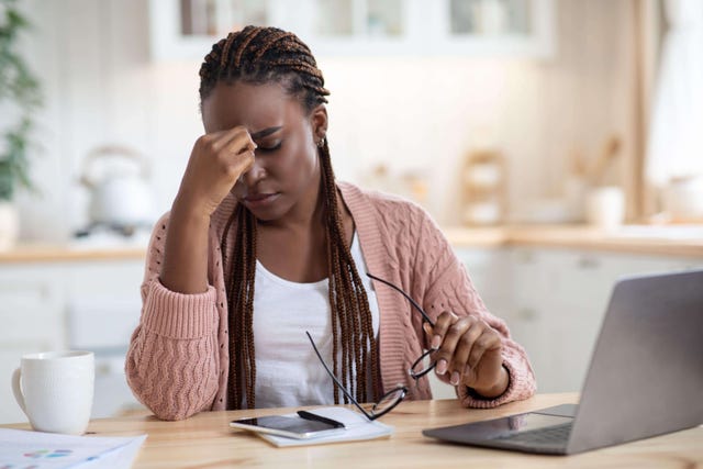 Overworked Black woman massages her eyes while using laptop in kitchen
