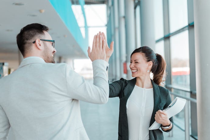 One person giving a high-five to another person in an office setting.