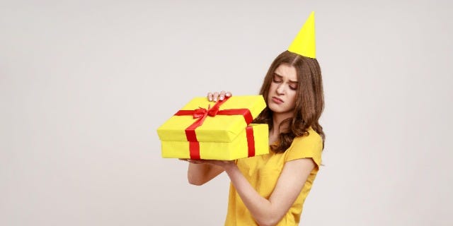 Upset teenager girl opening birthday gift box and looking inside with disappointed expression, unwrapping bad present
