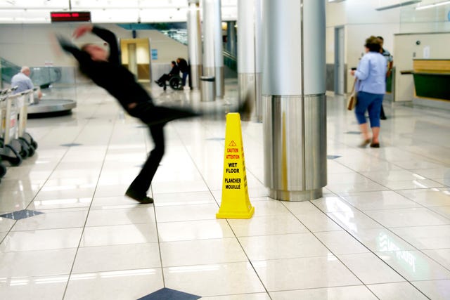 A subway station with a wet floor sign and someone slipping and falling, blurry in midair