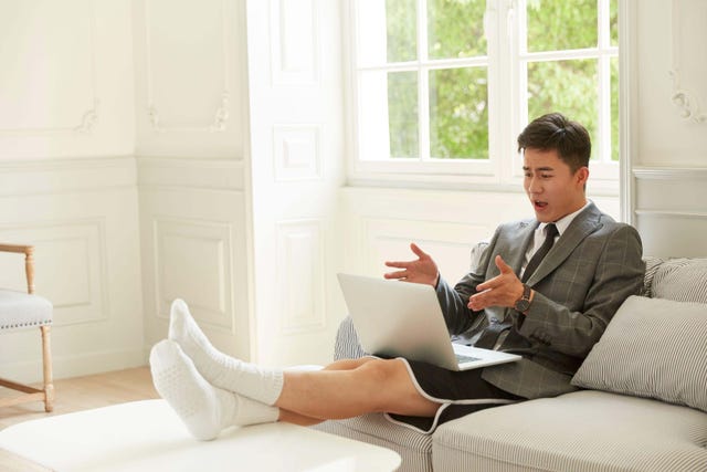 young asian business man wearing suit and shorts working from home meeting with colleagues online using video chat on laptop