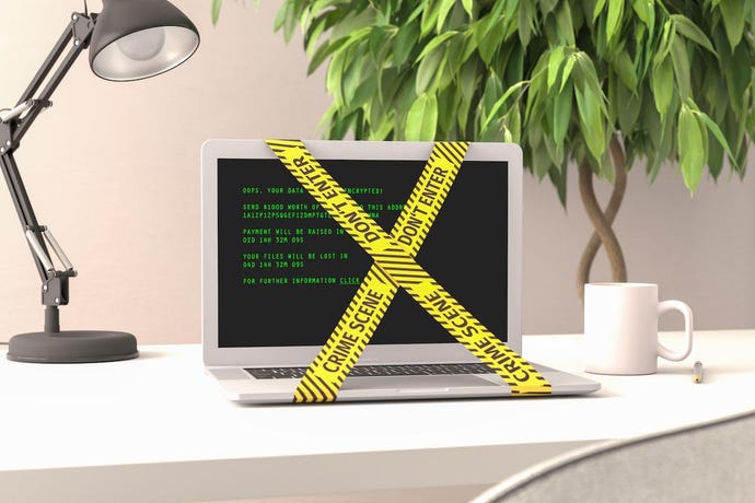 Image shows a couputer terminal with "crime scene" yellow tape around it, a lamp and a plant on an office desk;