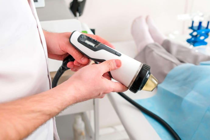 A medical professional holds a urology device while a clothed patient awaits in the background